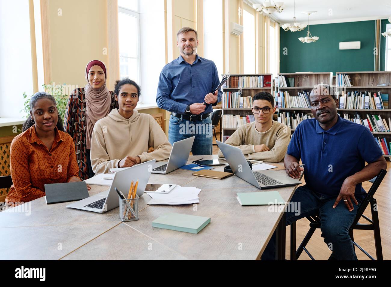 Group portrait of modern English language teacher and multi-ethnic immigrant students having class in library looking at camera Stock Photo