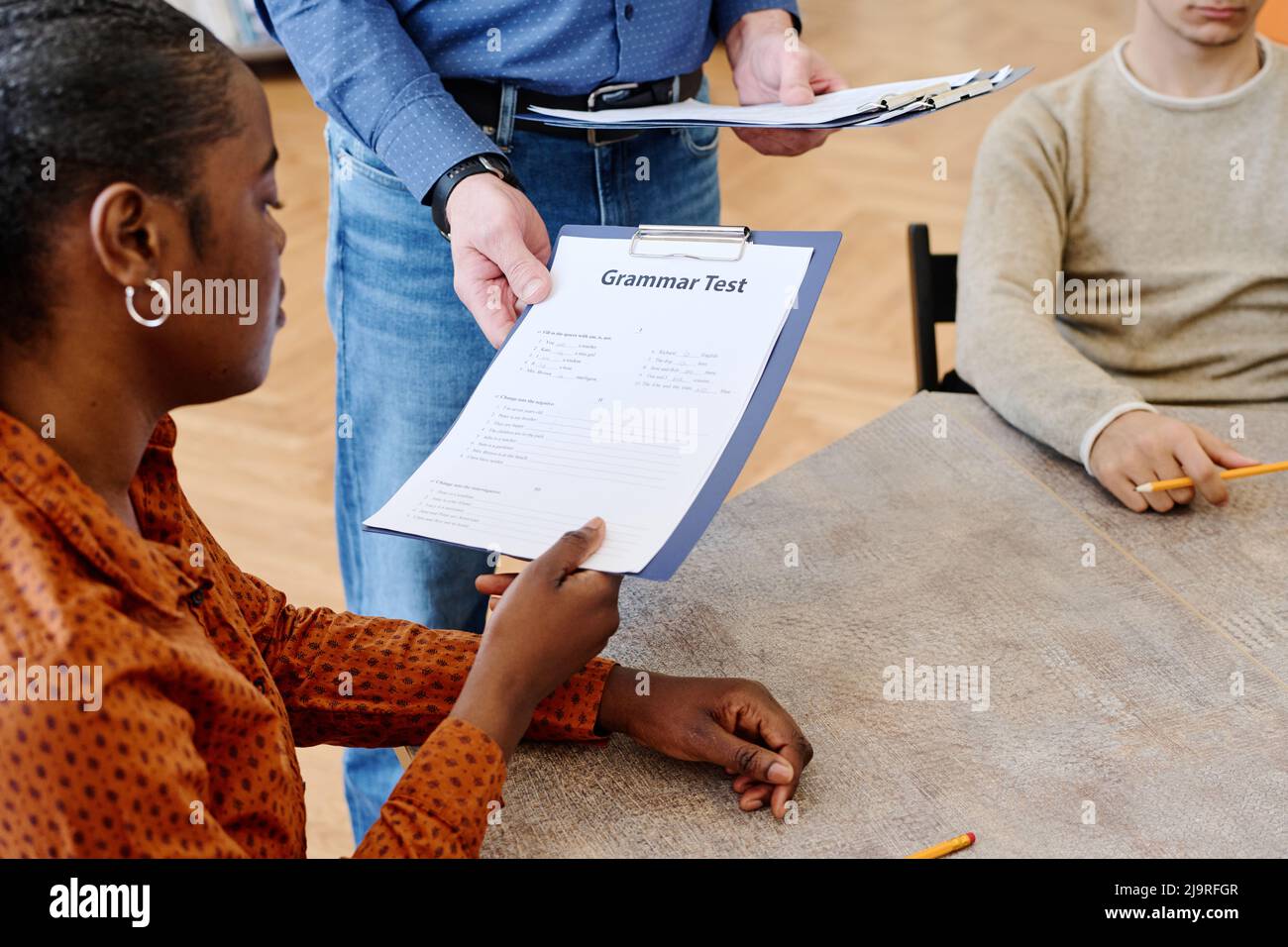 Young Black woman learning English at school for immigrants finishing grammar test and giving it to teacher Stock Photo