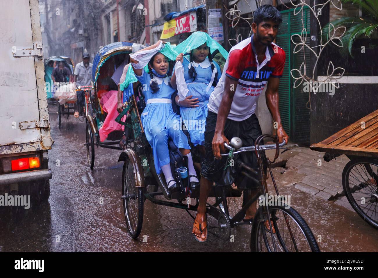 Children wearing school dress protect their heads from rain with polythene while riding on a rickshaw in Dhaka, Bangladesh, May 25, 2022. REUTERS/Mohammad Ponir Hossain Stock Photo