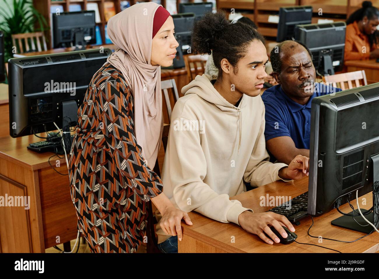Group of three immigrant students spending in modern library searching something together in internet on computer Stock Photo