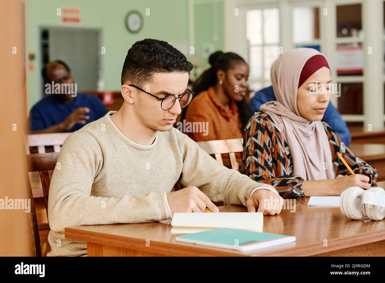 Group of immigrant students in international class sitting at desk reading and making notes during lesson Stock Photo