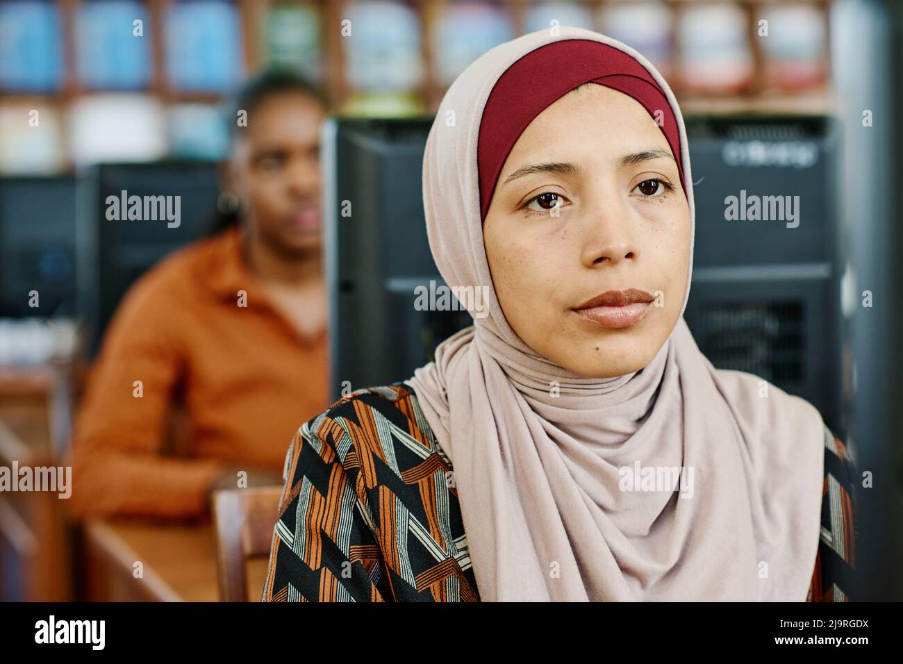 Portrait of young Muslim woman wearing hijab sitting in university ...