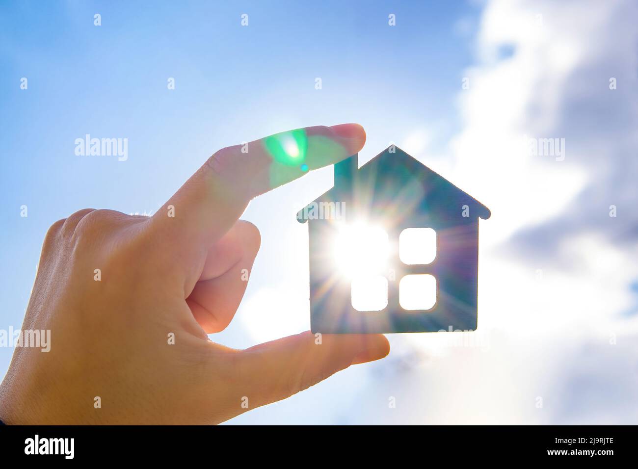 Hand holding a flat wooden house against sunny sky with sun rays Stock ...
