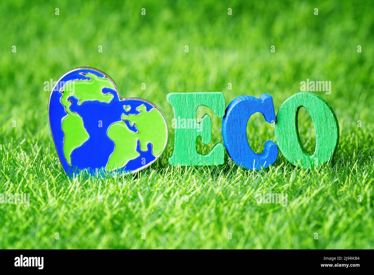 Word ECO made from wooden letters and a heart shaped world pin on a green grass background. Environment care concept. Stock Photo