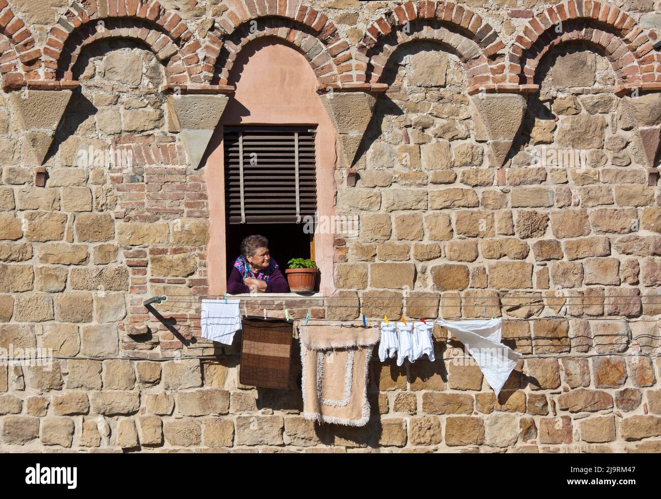 Italy, Tuscany, Siena Province, Buonconvento. Italian woman looking out her window with clothes hanging on line drying in the medieval village of Buon Stock Photo