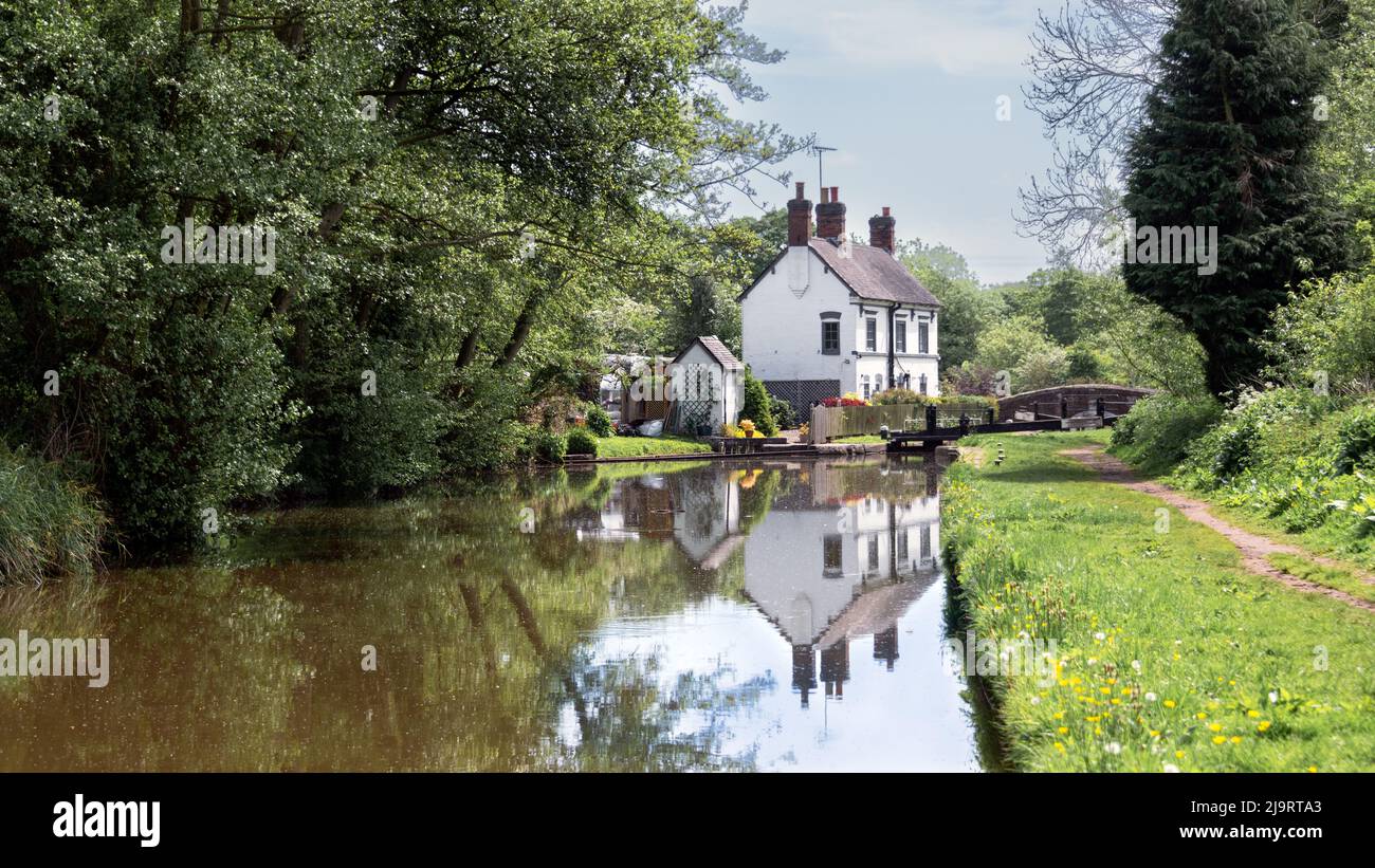 A summer canal scene of a lock keepers cottage on inland waterway. The old cottage is reflected in the still water Stock Photo