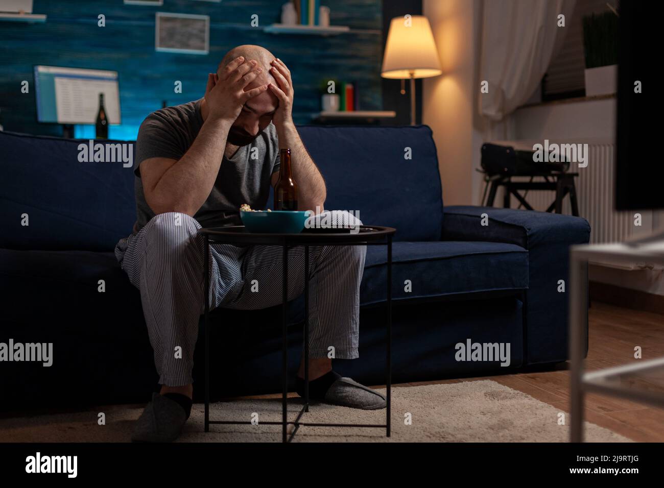 Frustrated man watching sports on television program and feeling sad about football team losing championship game. Soccer supporter fan feeling upset and emotional about match defeat. Stock Photo