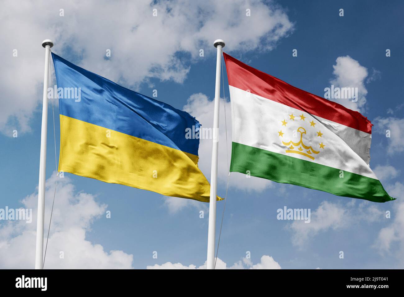 Ukraine and Tajikistan two flags on flagpoles and blue cloudy sky background Stock Photo