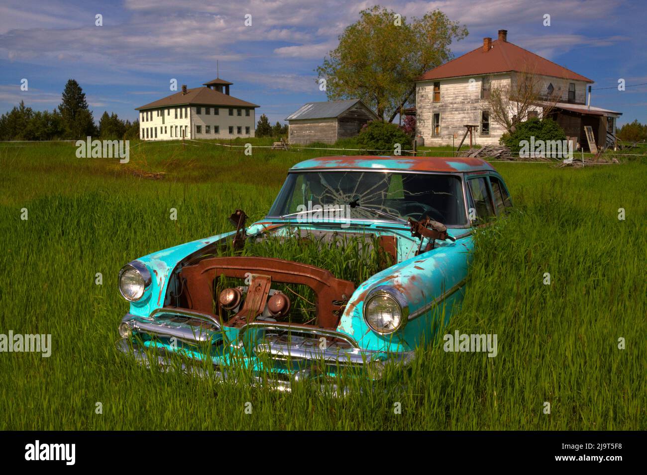 USA, Oregon. Old car in field of grass with old abandoned Flora School