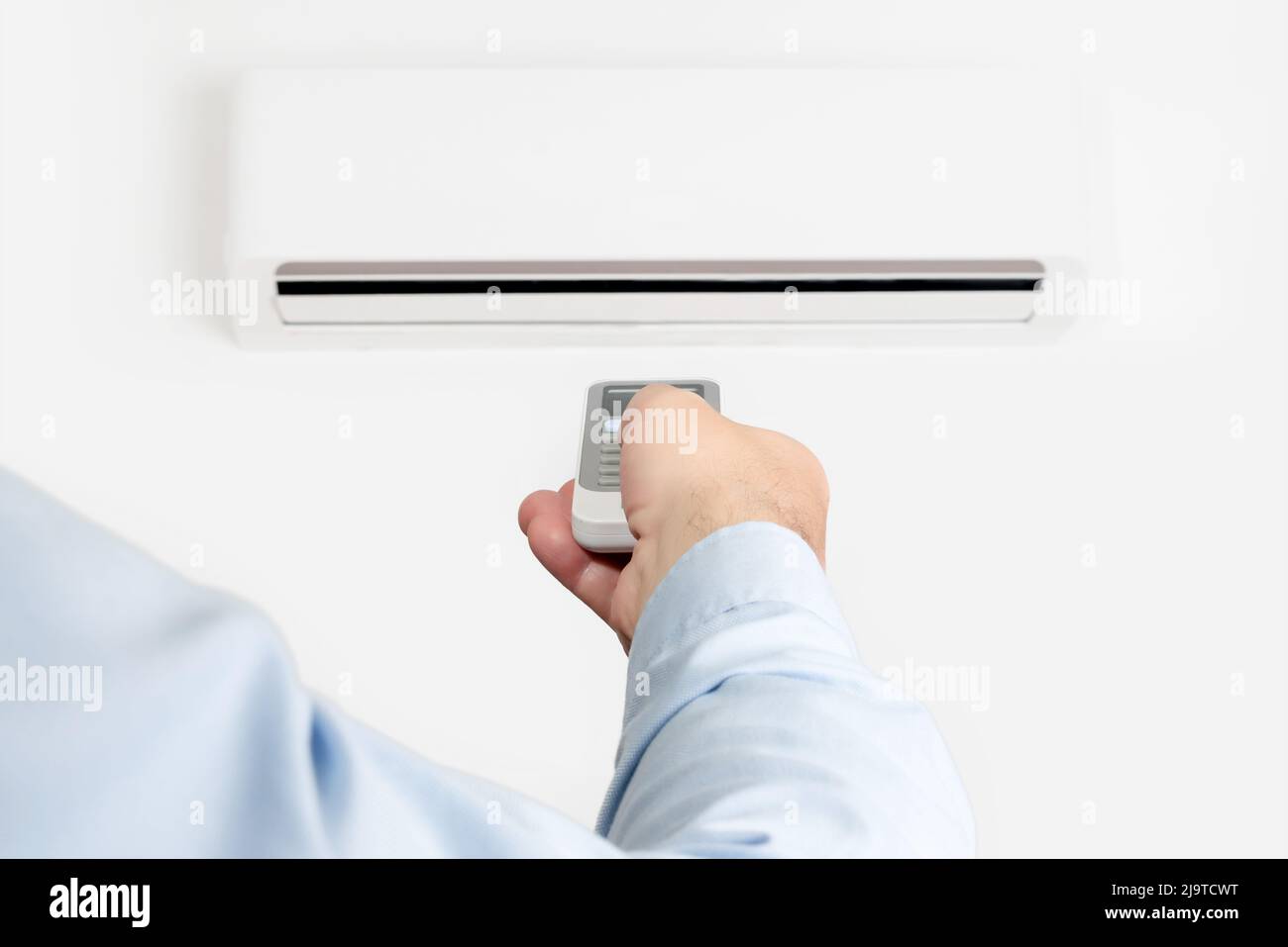 A man pointing a remote control at an air conditioner. Turning on the