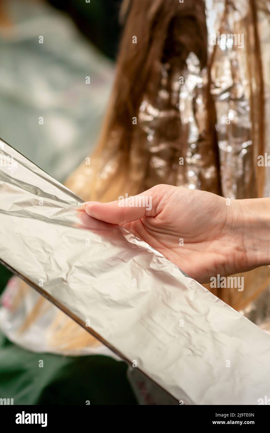 Hairdresser's Hands Holding Foil Sheet For Hair Dye In Beauty Salon