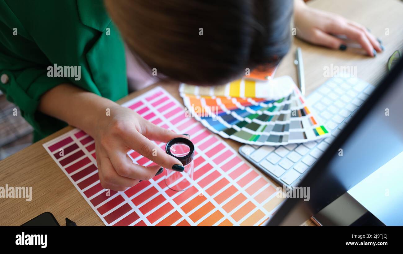 Designer looks through magnifying glass at samples of colors and shades of red on paper palette Stock Photo