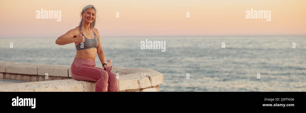 Asian lady in sportswear sitting on the edge of seafront Stock Photo