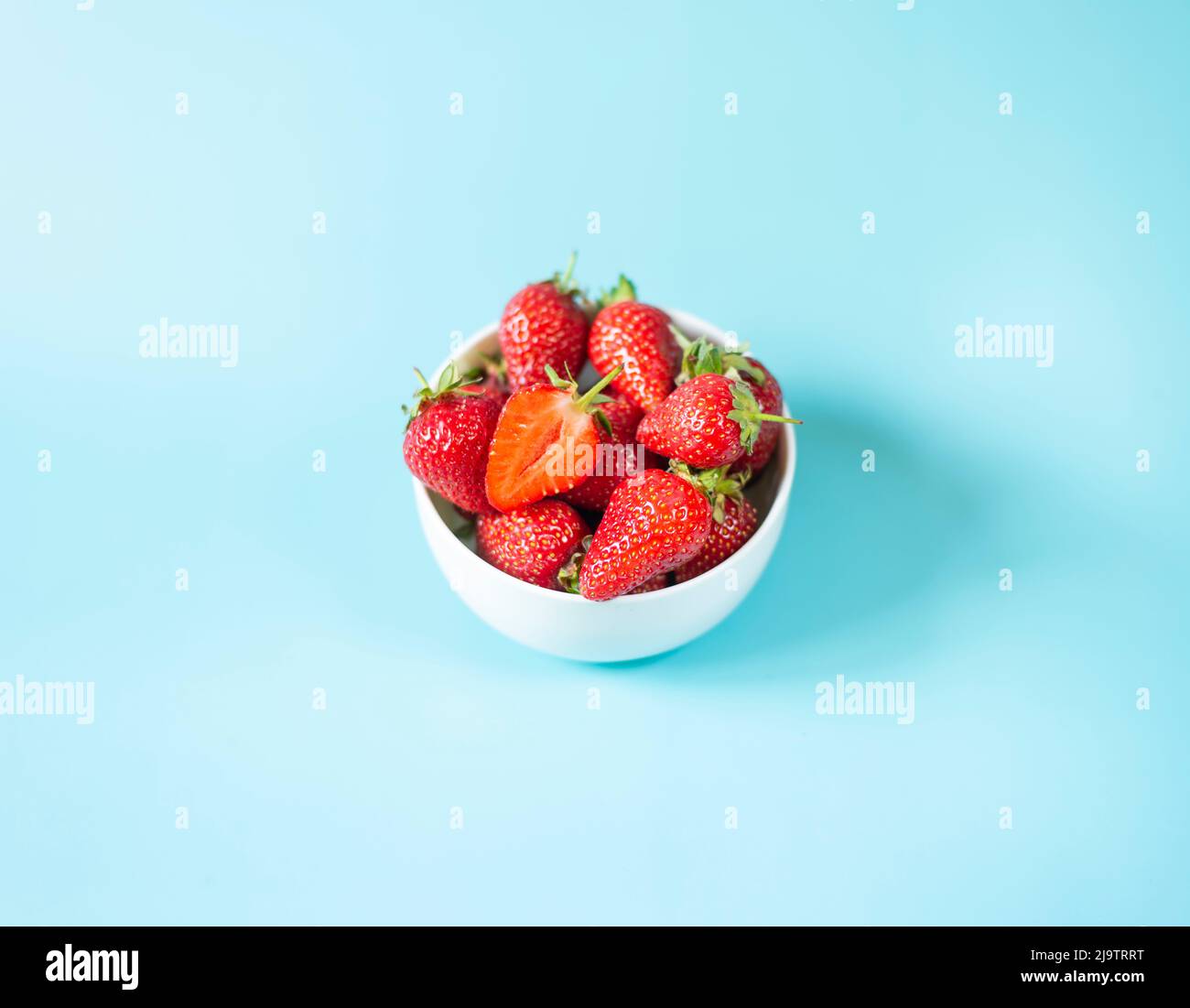 Fresh organic and juicy strawberries in pot on light blue background ...