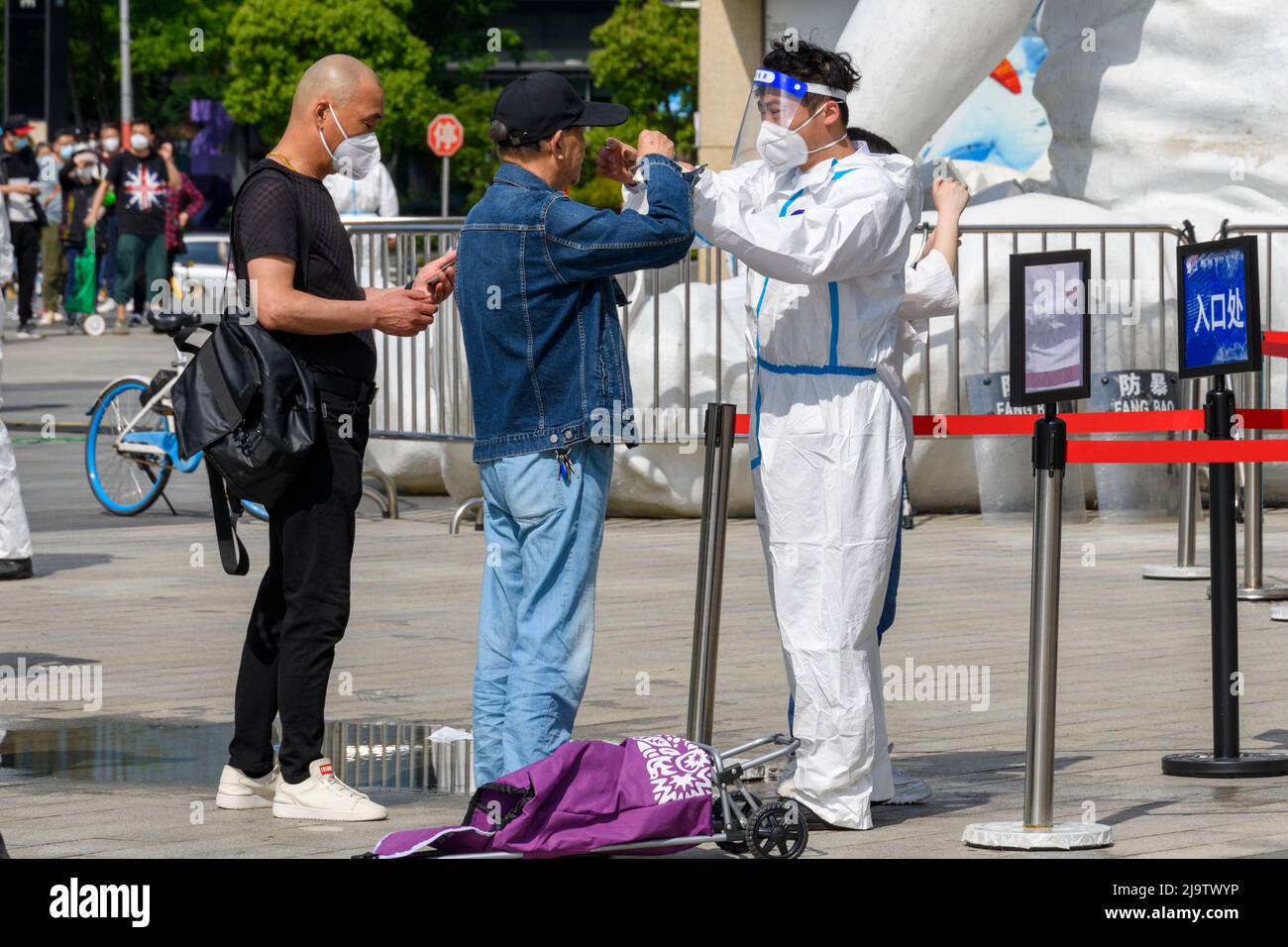 One of the health inspector assists an elderly man in putting his N-95 mask on as he waits in line to go shopping during the Shanghai lockdown. Stock Photo