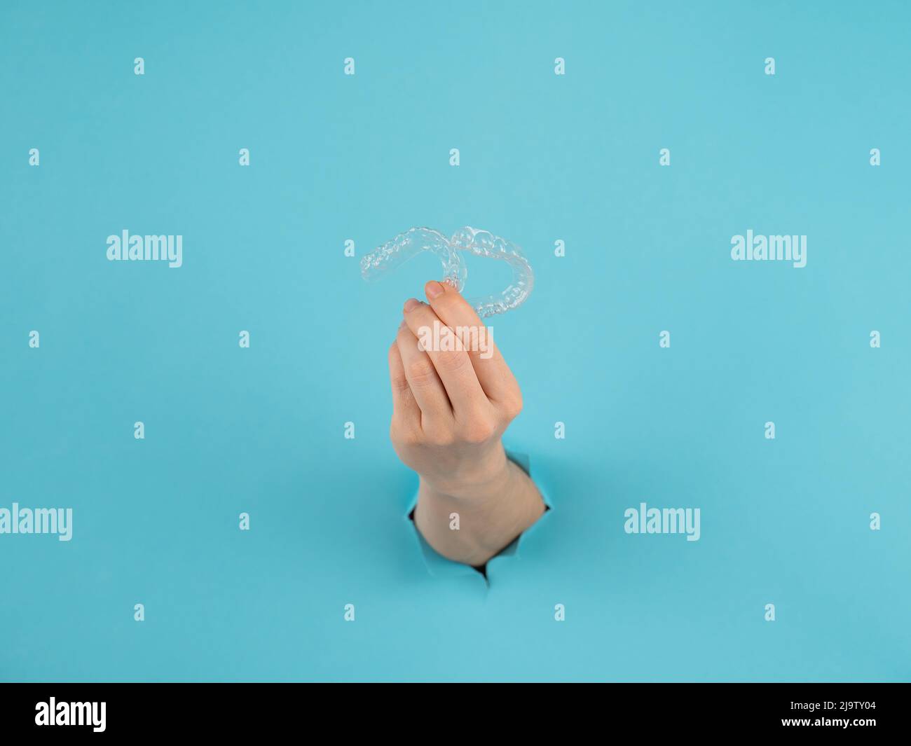 A female hand sticking out of a hole from a blue background holds ...