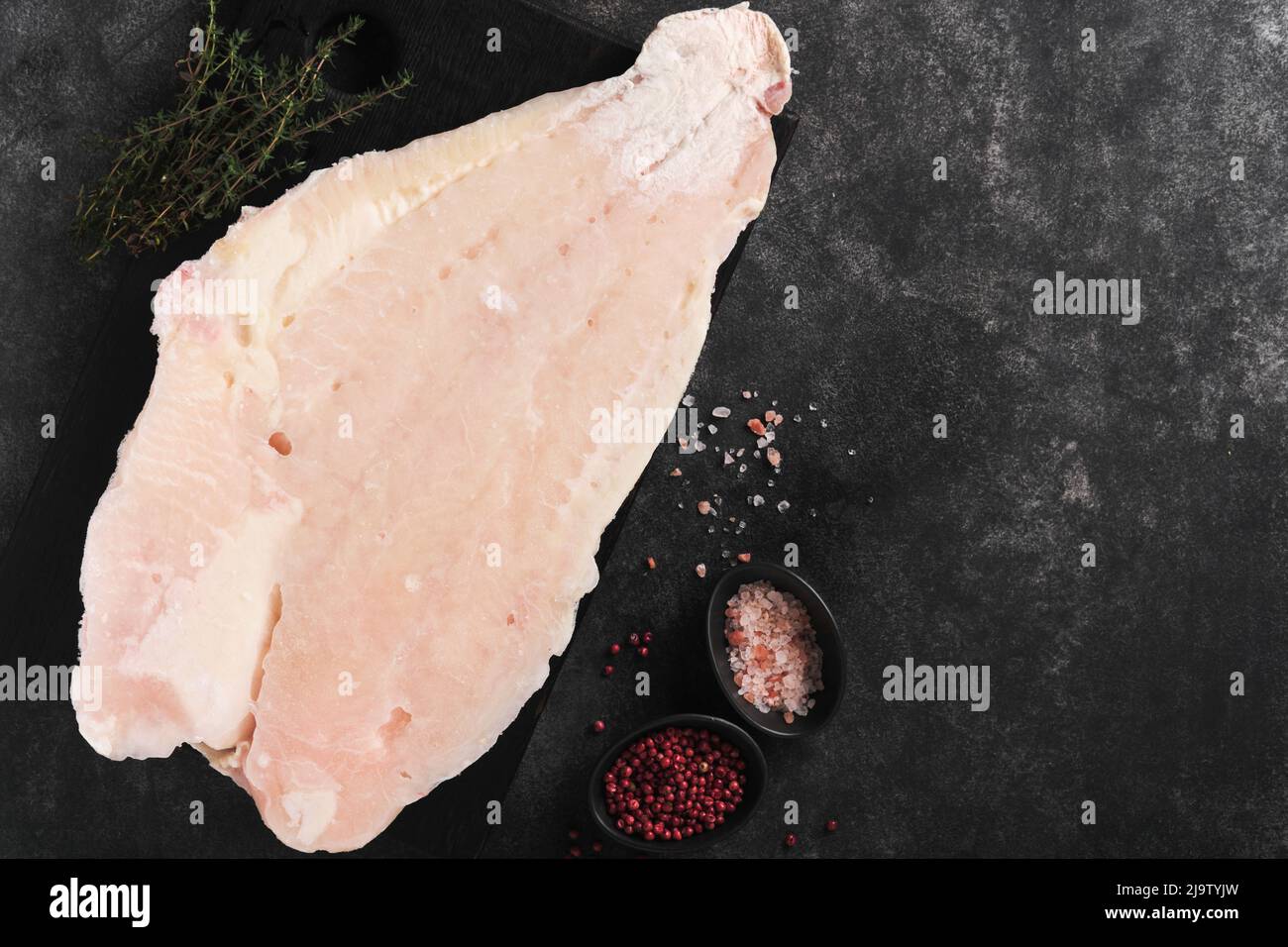 Pangasius frozen fillet. Raw fillet of white fish catfish. Pangasius with spices. Black background. Top view. Stock Photo