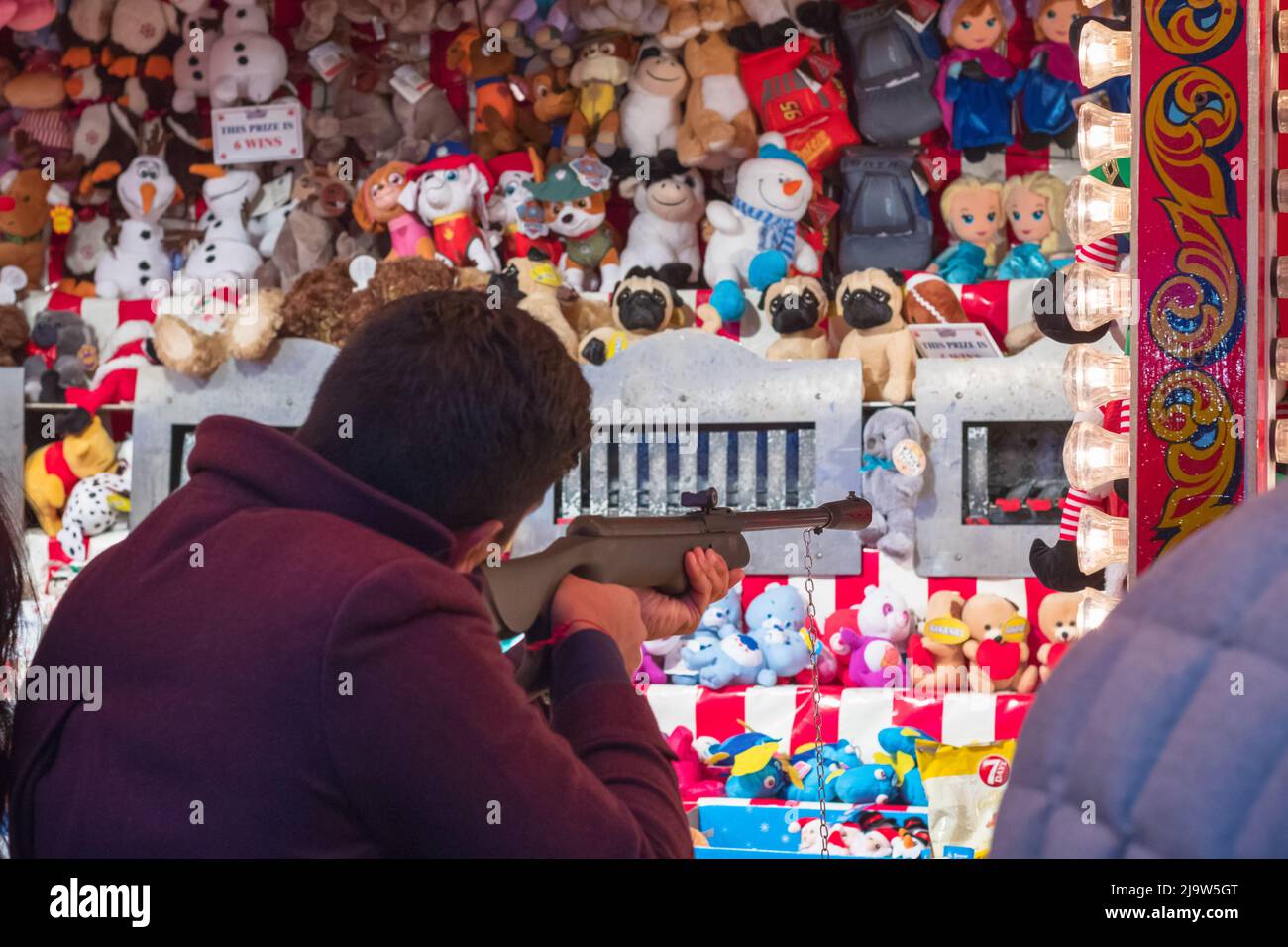 London, UK - December 2, 2021 - Tourist playing shooting game to win stuffed toys on the wall at Christmas funfair Hyde Park Winter Wonderland Stock Photo