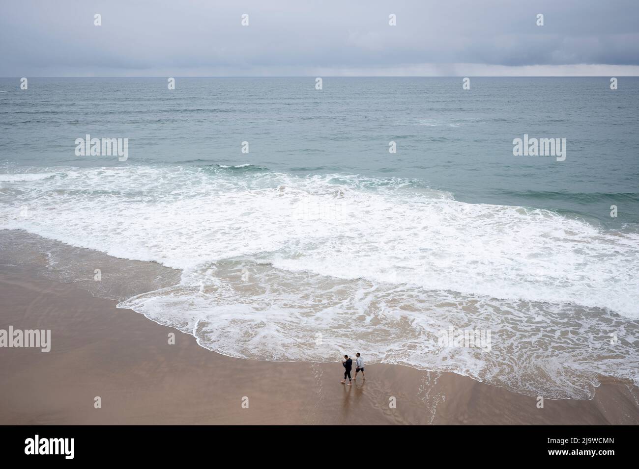 Beach surf walkers get wet in the coastal waters of the Bay of Biscay, on 12th May 2022, in Comillas, Cantabria, Spain. Stock Photo