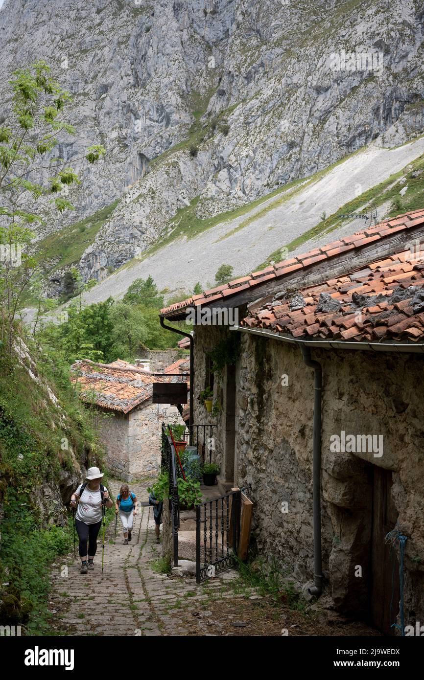 Walkers pass through the Spanish mountain village of Bulnes, a popular Spanish hiking destination for visitors to the Picos de Europa National Park, on 15th May 2022, at Bulnes, Picos Mountains, Asturias, Spain. Reached by path or by funicular railway, the tiny village of Bulnes provides beds and food to passing walkers. Stock Photo