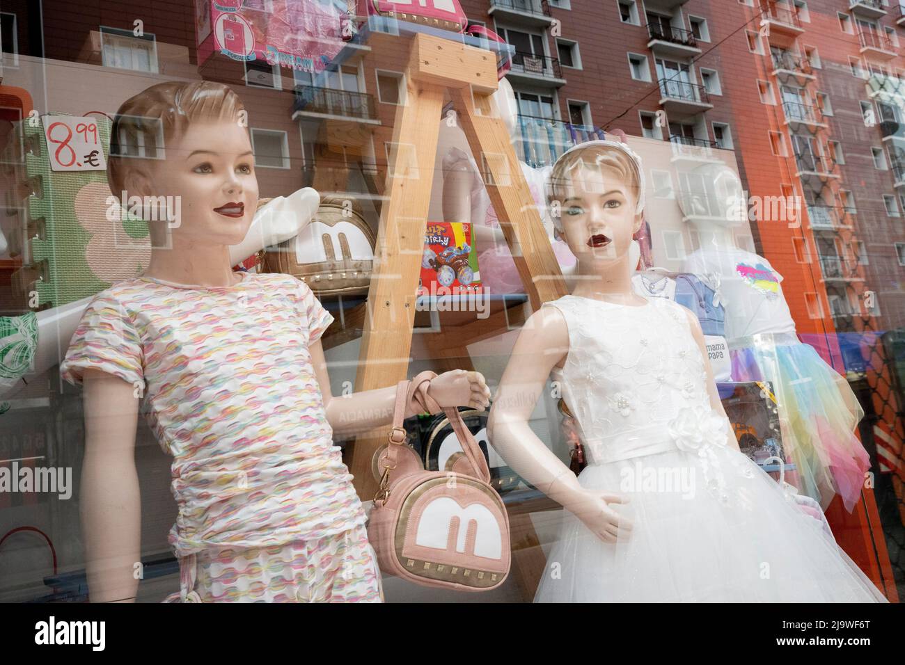 With residential apartments reflected in the background, childrens' mannequins are seen in a clothing retailer's window in central Bilbao, on 21st May 2022, in Bilbao, Cantabria, Spain. Stock Photo