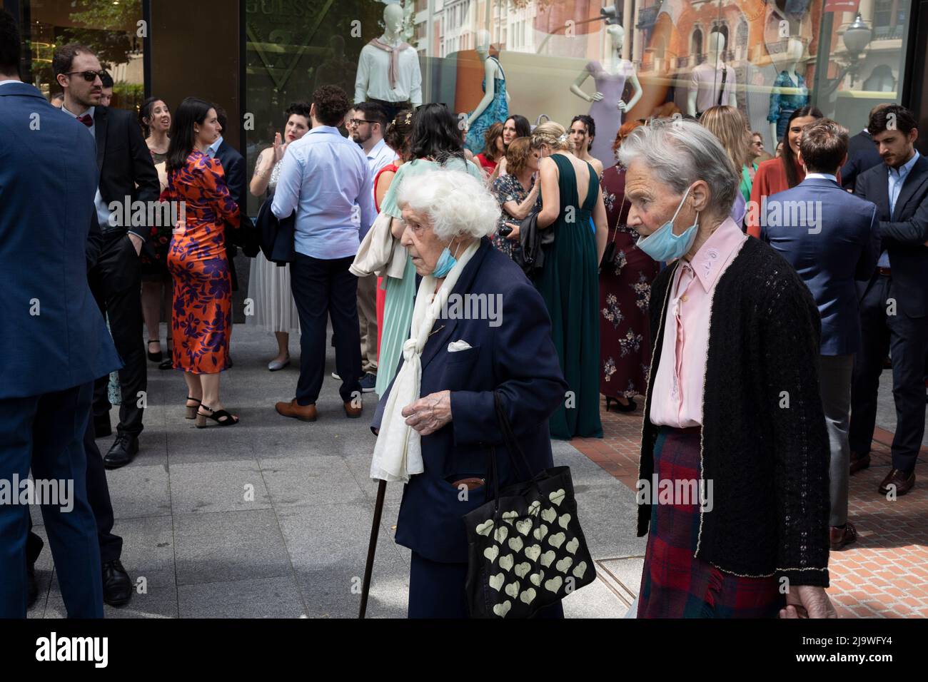 Elderly Spanish women walk past guests of a wedding outside a clothing retailer on 'Gran via Don Diego Lopez de Haro' in central Bilbao, on 21st May 2022, in Bilbao, Cantabria, Spain. Stock Photo