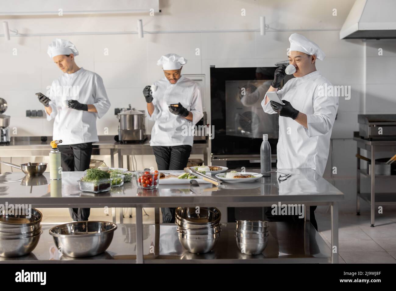 Group of cooks using phones and drinking coffee during a break in the