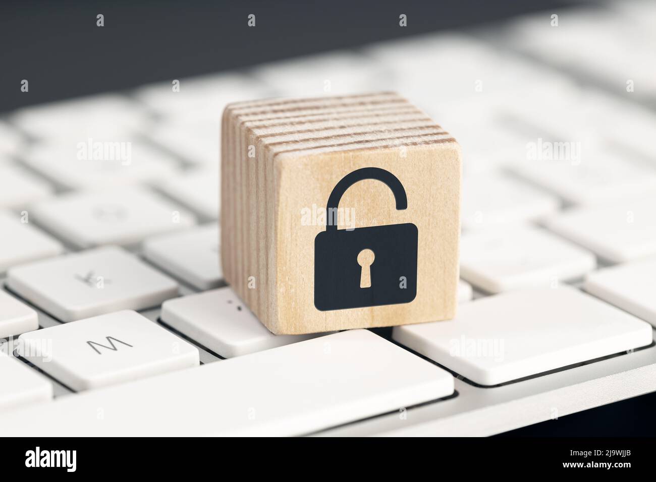 Computer security risk concept. Open padlock icon on wooden cube on computer keyboard Stock Photo