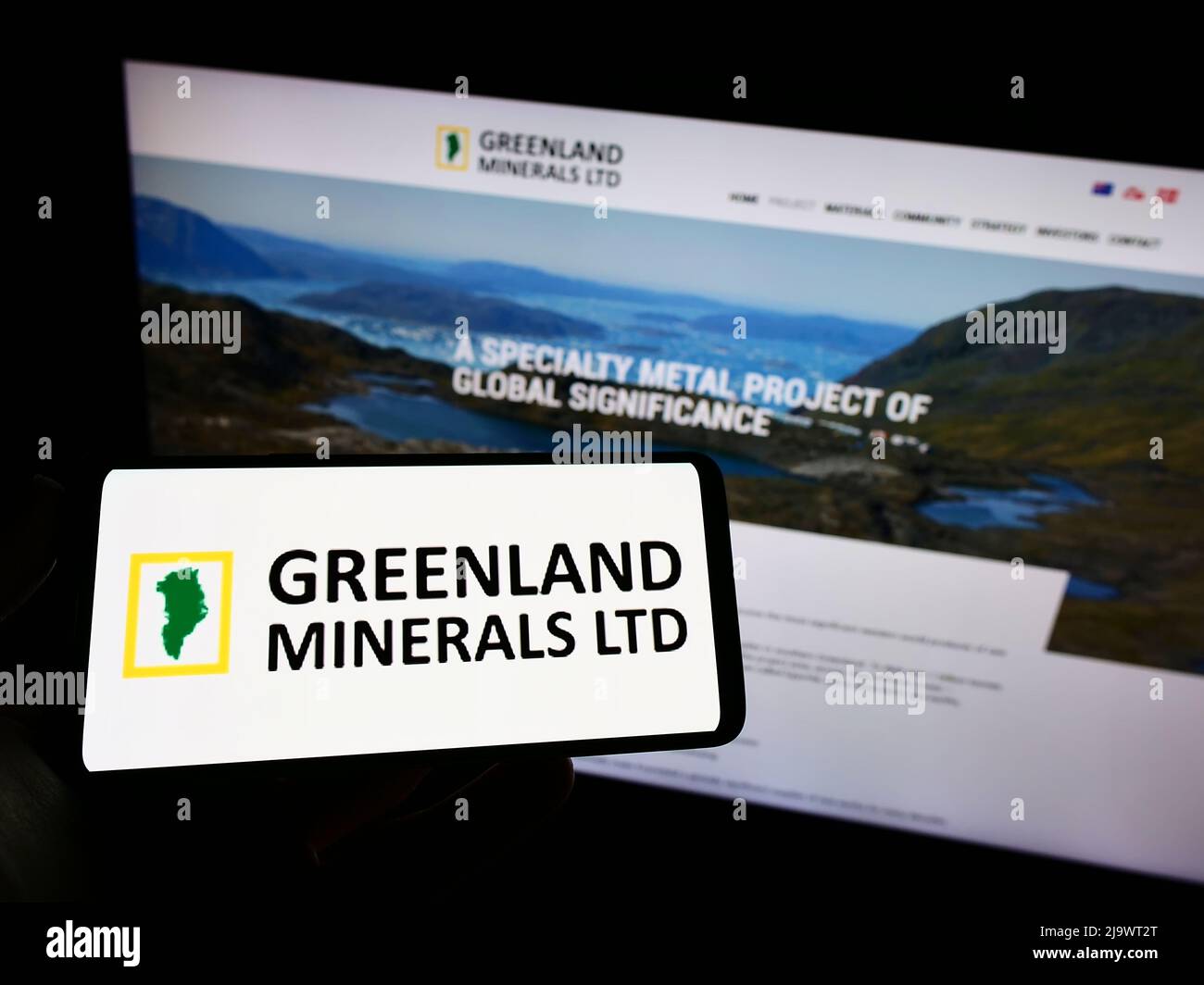Person holding smartphone with logo of mining company Greenland Minerals Limited on screen in front of website. Focus on phone display. Stock Photo