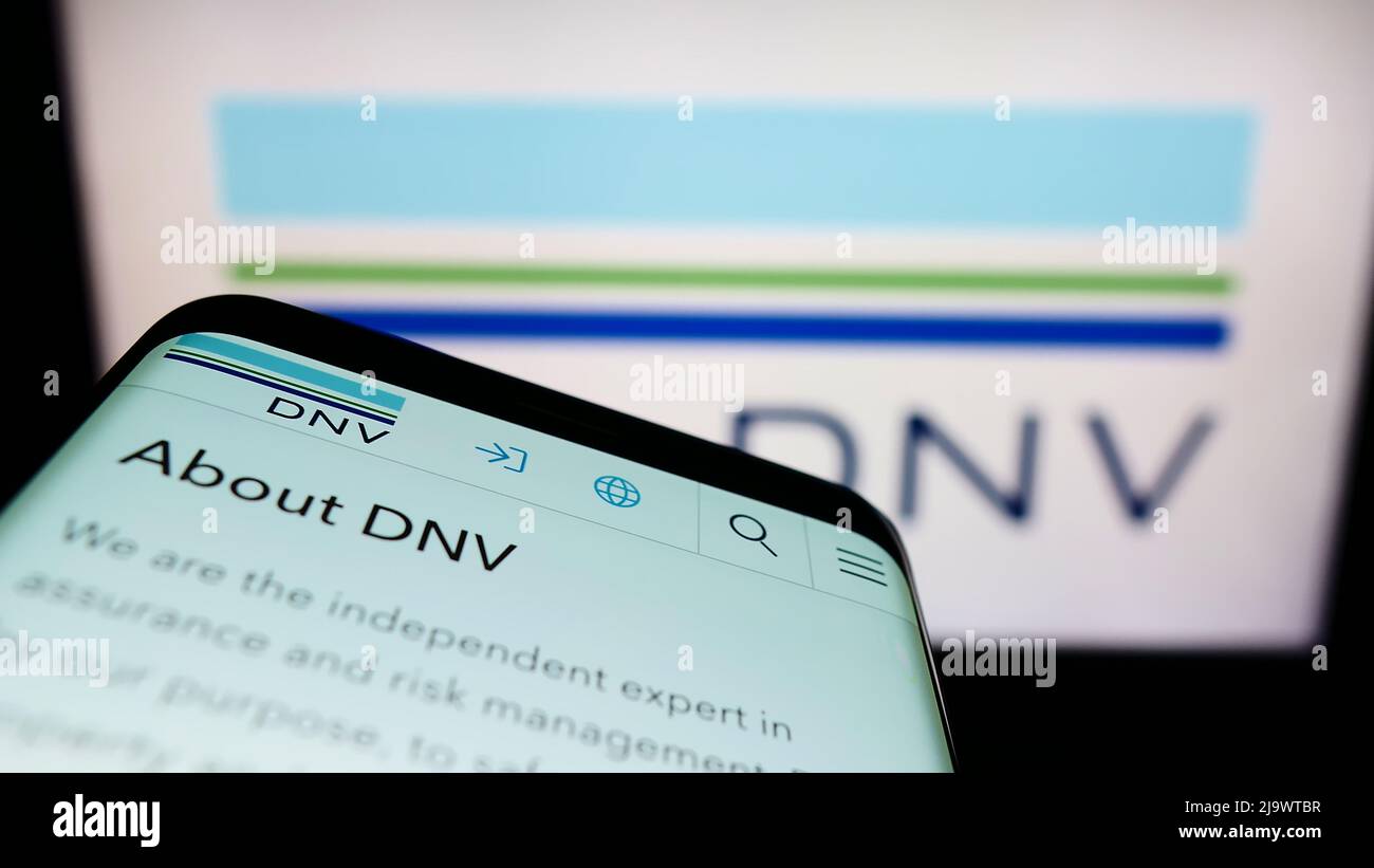Smartphone with website of Norwegian services company DNV AS on screen in front of business logo. Focus on top-left of phone display. Stock Photo