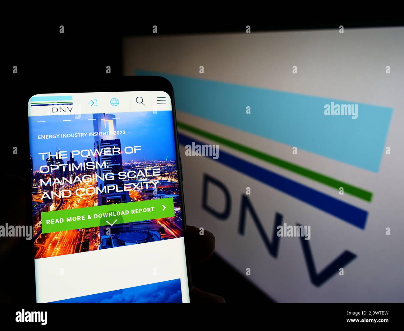 Person holding cellphone with webpage of Norwegian services company DNV AS on screen in front of business logo. Focus on center of phone display. Stock Photo