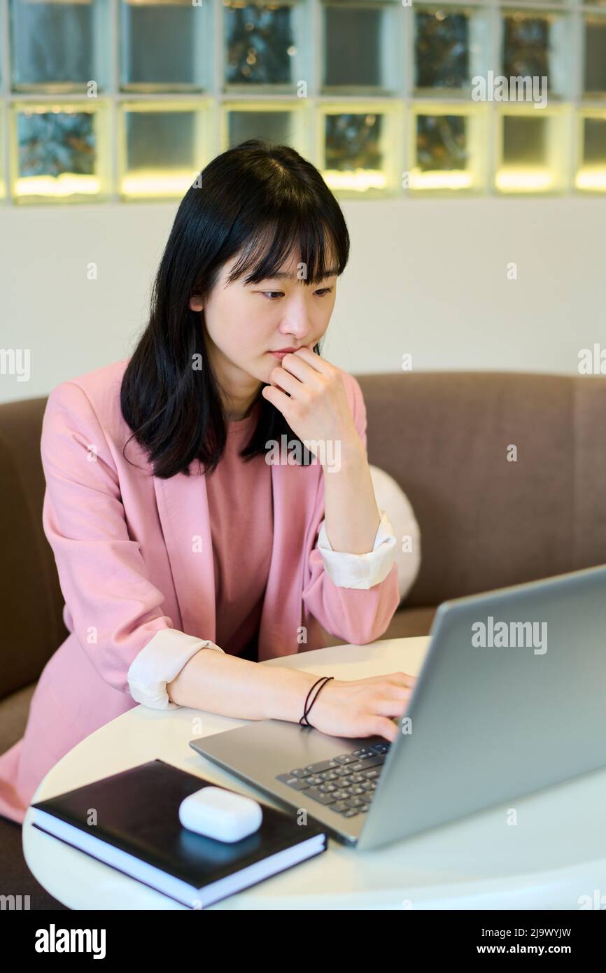 Young female freelancer sitting at table in cafe looking at monitor with pensive expression during her online work at cafe Stock Photo