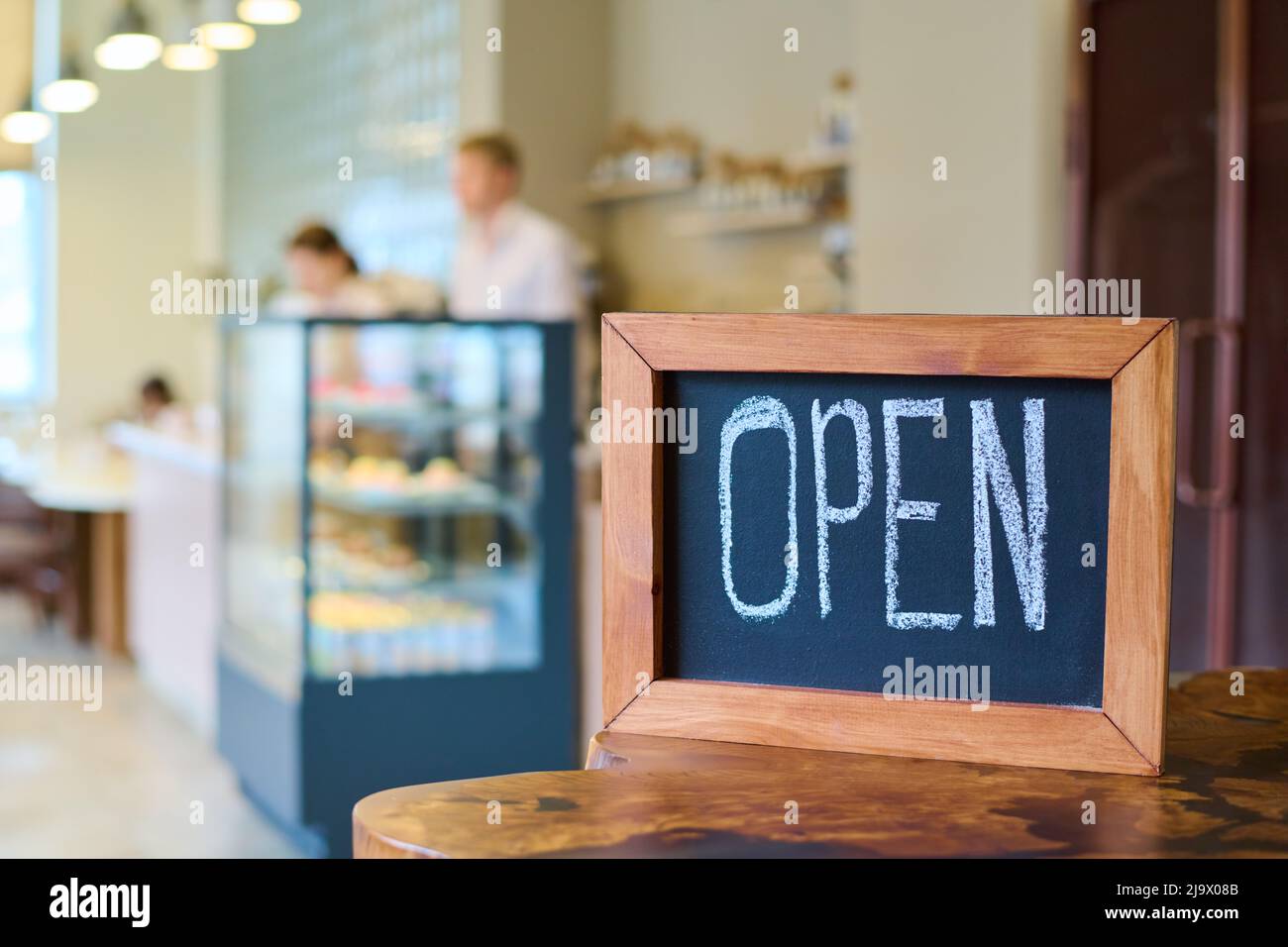 Close-up of wooden board with open sign written by chalk on table in coffee shop Stock Photo