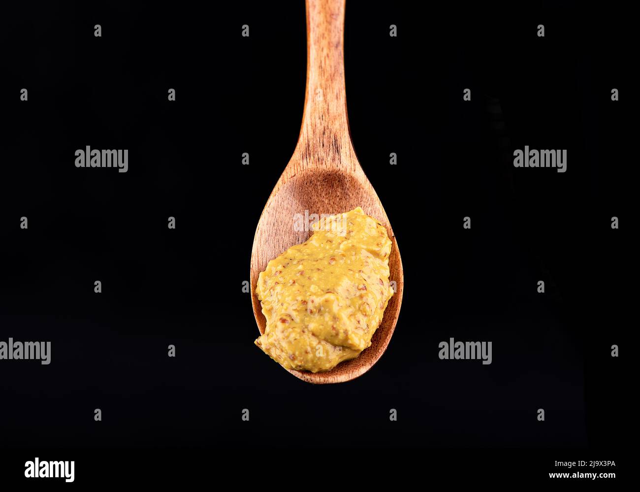 Close-up of a wooden spoon with french mustard on a black background. Copy space. Stock Photo