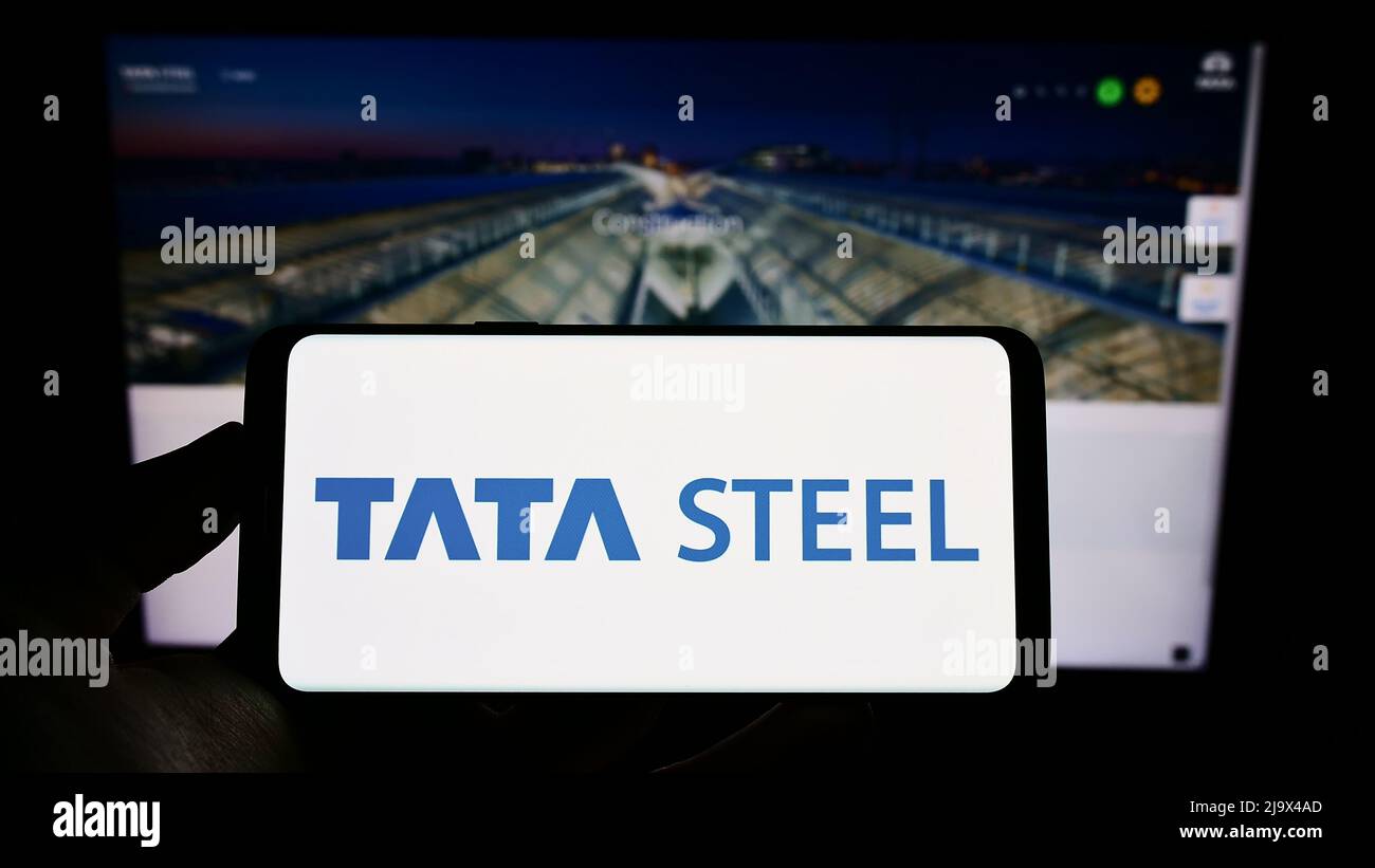 Person holding cellphone with logo of Indian steelmaking company Tata Steel Limited on screen in front of webpage. Focus on phone display. Stock Photo