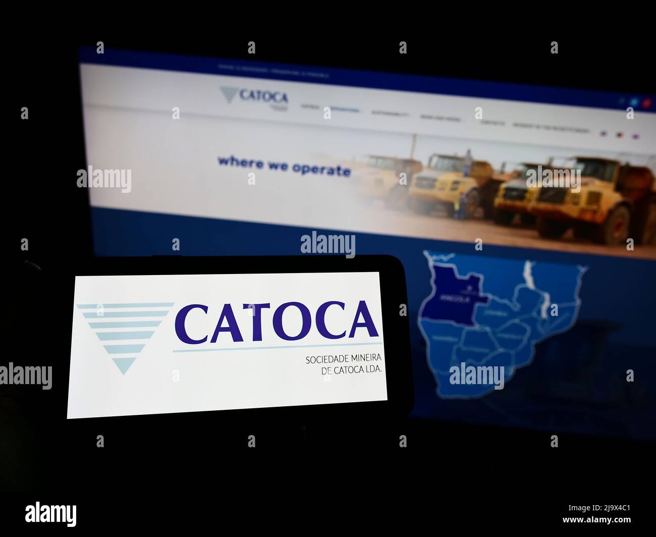 Person holding smartphone with logo of mining company Sociedade Mineira de Catoca Lda. on screen in front of website. Focus on phone display. Stock Photo