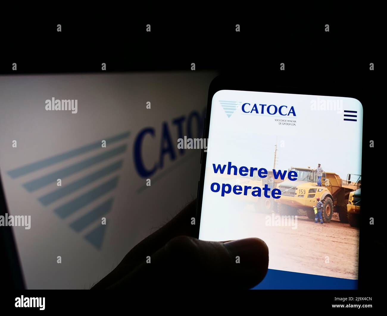 Person holding cellphone with website of mining company Sociedade Mineira de Catoca Lda. on screen in front of logo. Focus on center of phone display. Stock Photo