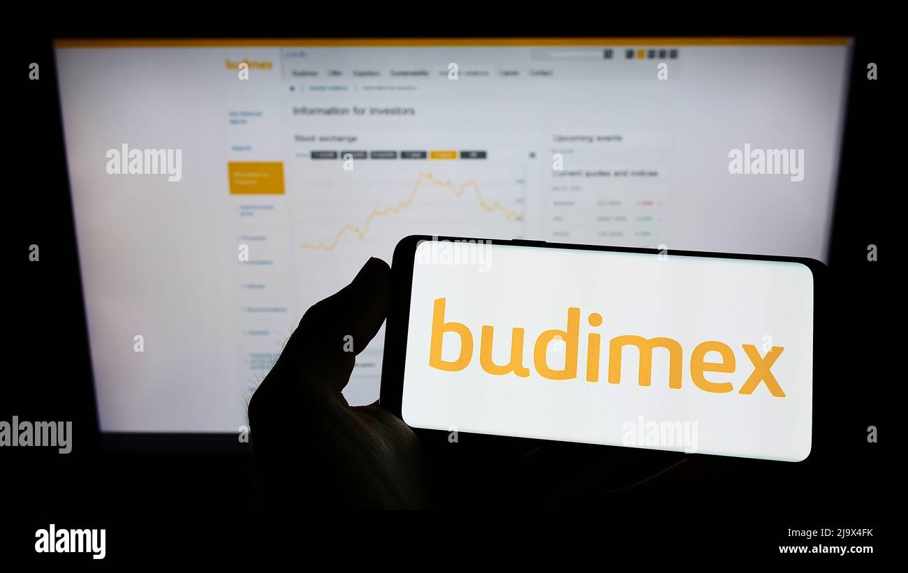 Person holding mobile phone with logo of Polish construction company Budimex SA on screen in front of business web page. Focus on phone display. Stock Photo