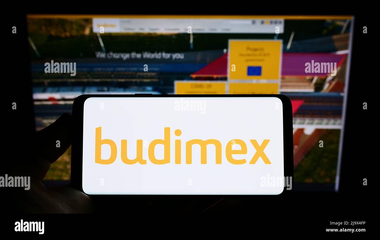 Person holding smartphone with logo of Polish construction company Budimex S.A. on screen in front of website. Focus on phone display. Stock Photo