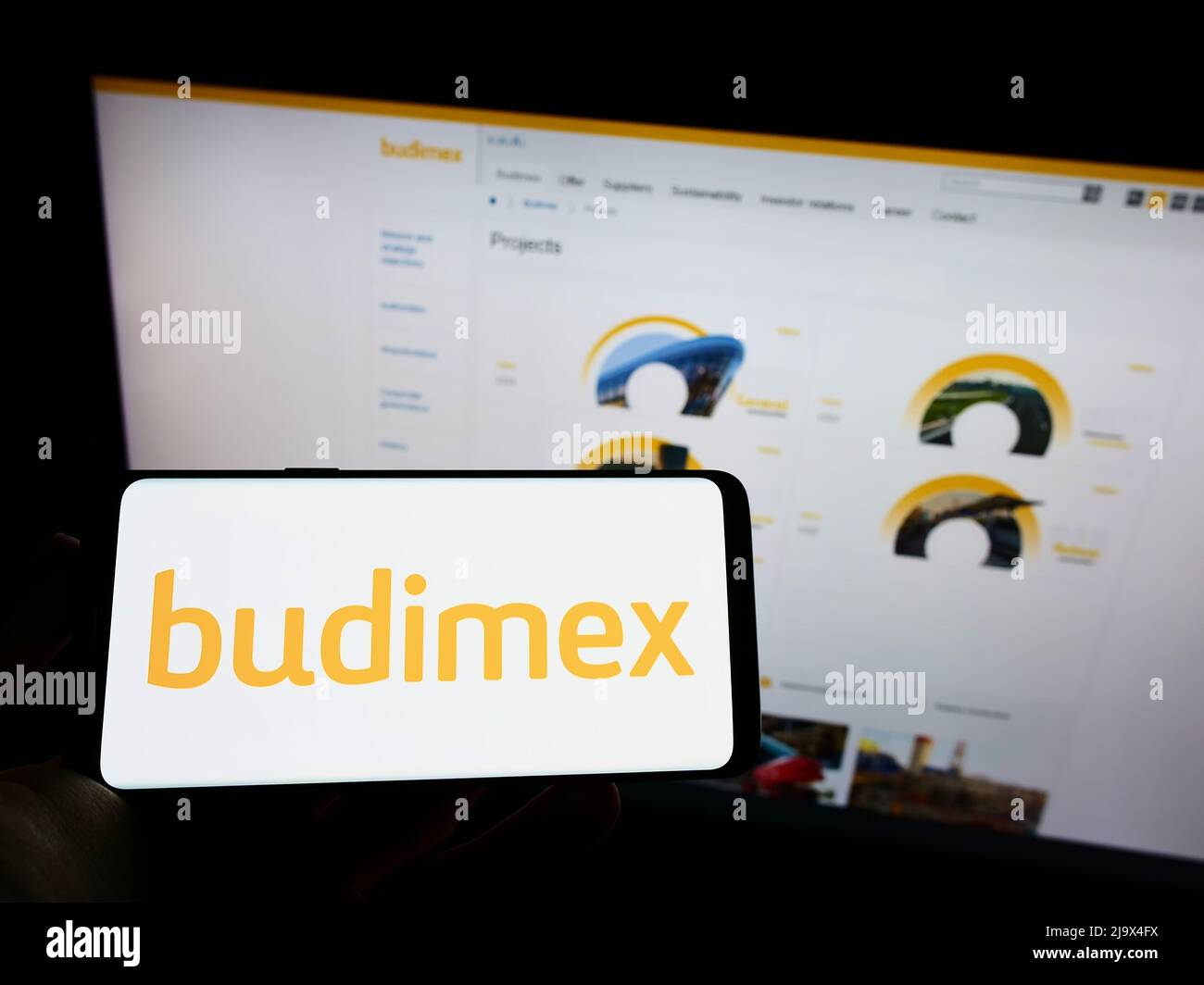 Person holding cellphone with logo of Polish construction company Budimex S.A. on screen in front of business webpage. Focus on phone display. Stock Photo