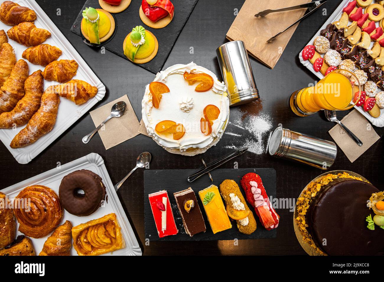 Set of desserts and cake on a black table, cream chocolate, icing sugar, butter croissants, orange juice, tea cakes, sweet snails. Stock Photo
