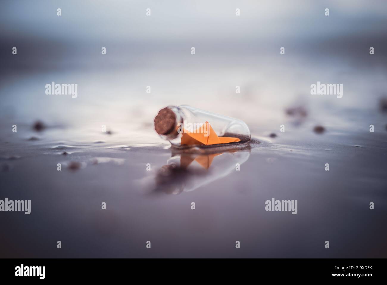 Miniature origami ship in bottle standing on sand at sunrise Stock Photo