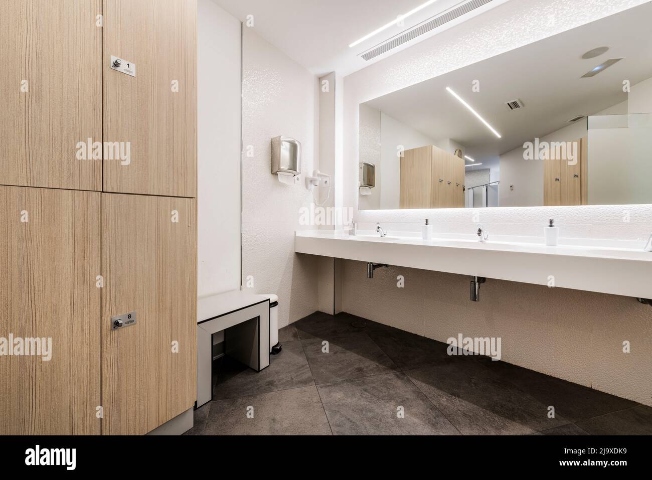 Restroom of a gym locker room with a wooden locker cabinet and a white resin washbasin with a mirror integrated into the wall Stock Photo
