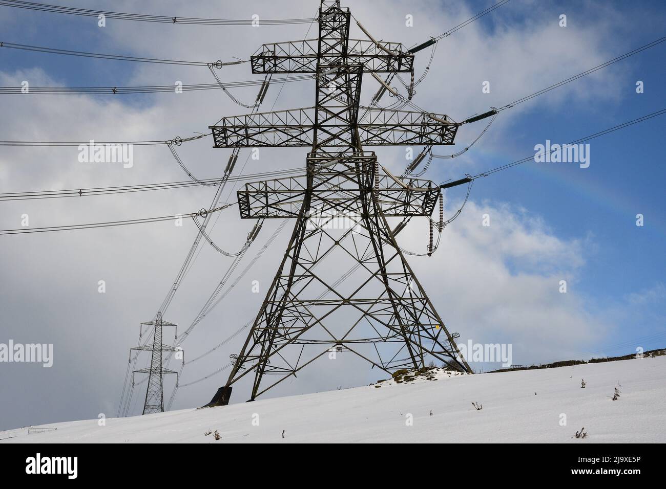 Electricity pylons on the moors above Stocksbridge near Sheffield, running across the Woodhead Pass towards Manchester in Winter with snow on the grou Stock Photo