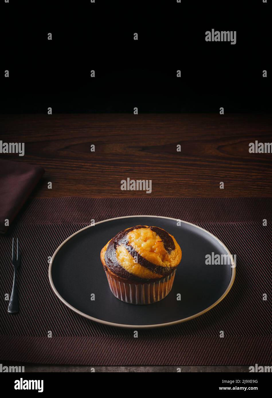 Vanilla Muffin with chocolate marbled on brown paper isolated on a thin plate on a nice table, fine pastries, Copy space Stock Photo