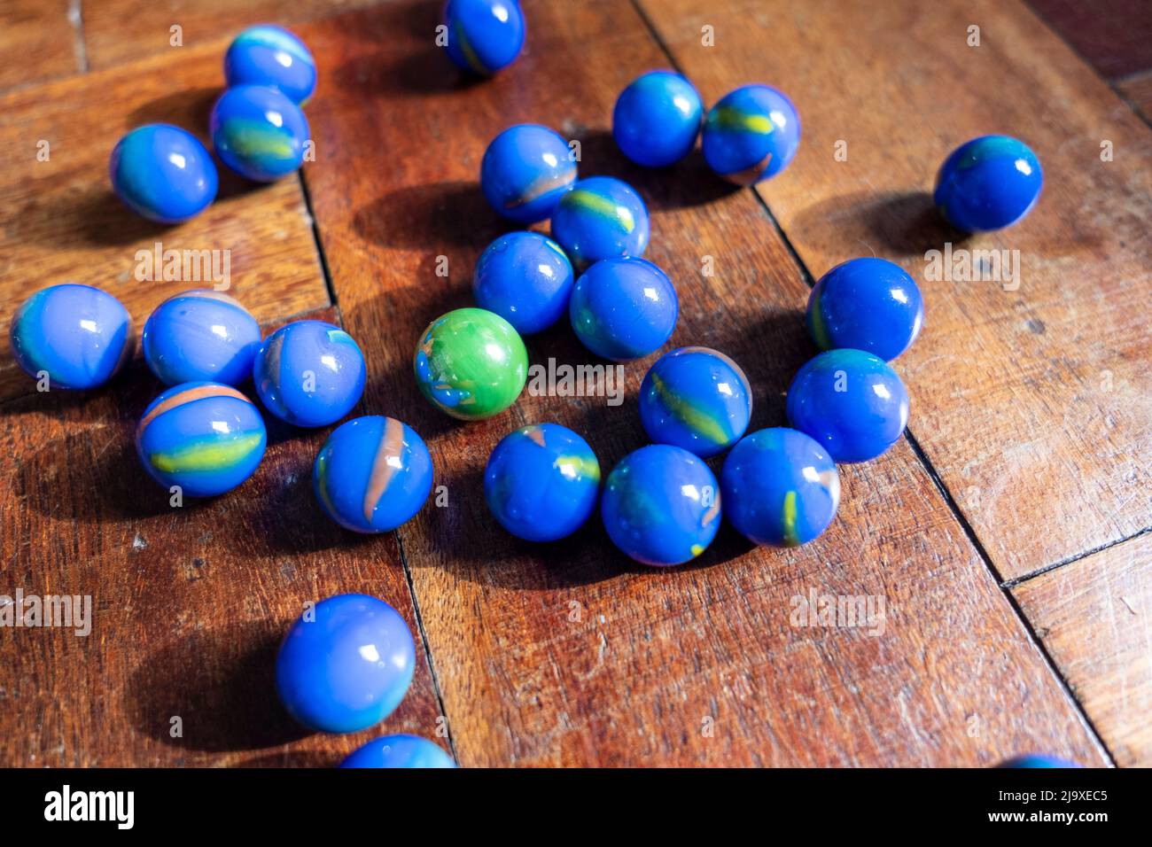 Blue marbles surrounding a green marble on a weathered wooden parquet floor Stock Photo