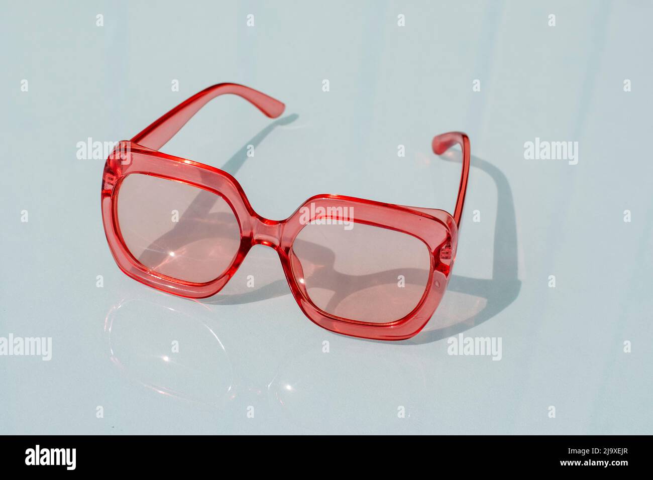 Red plastic sunglasses sitting on a glass table top Stock Photo