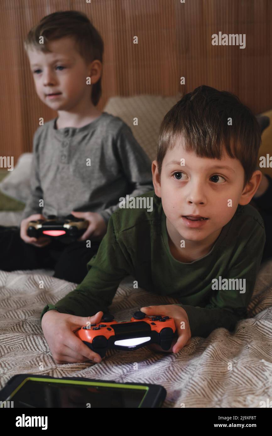 Kids playing video games at home on the bed at night. Boys using game console and having fun in the evening. Brothers using technologies exited. Boy Stock Photo