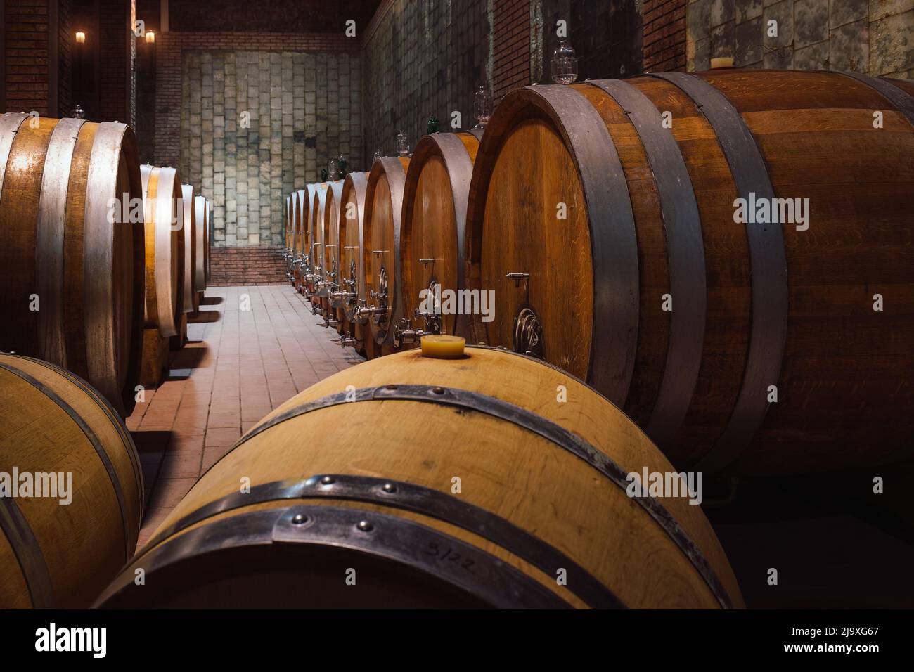 Underground dark cool arched wine cellar, storage room with large wooden barrels, placed in a line, deep focus. Stock Photo