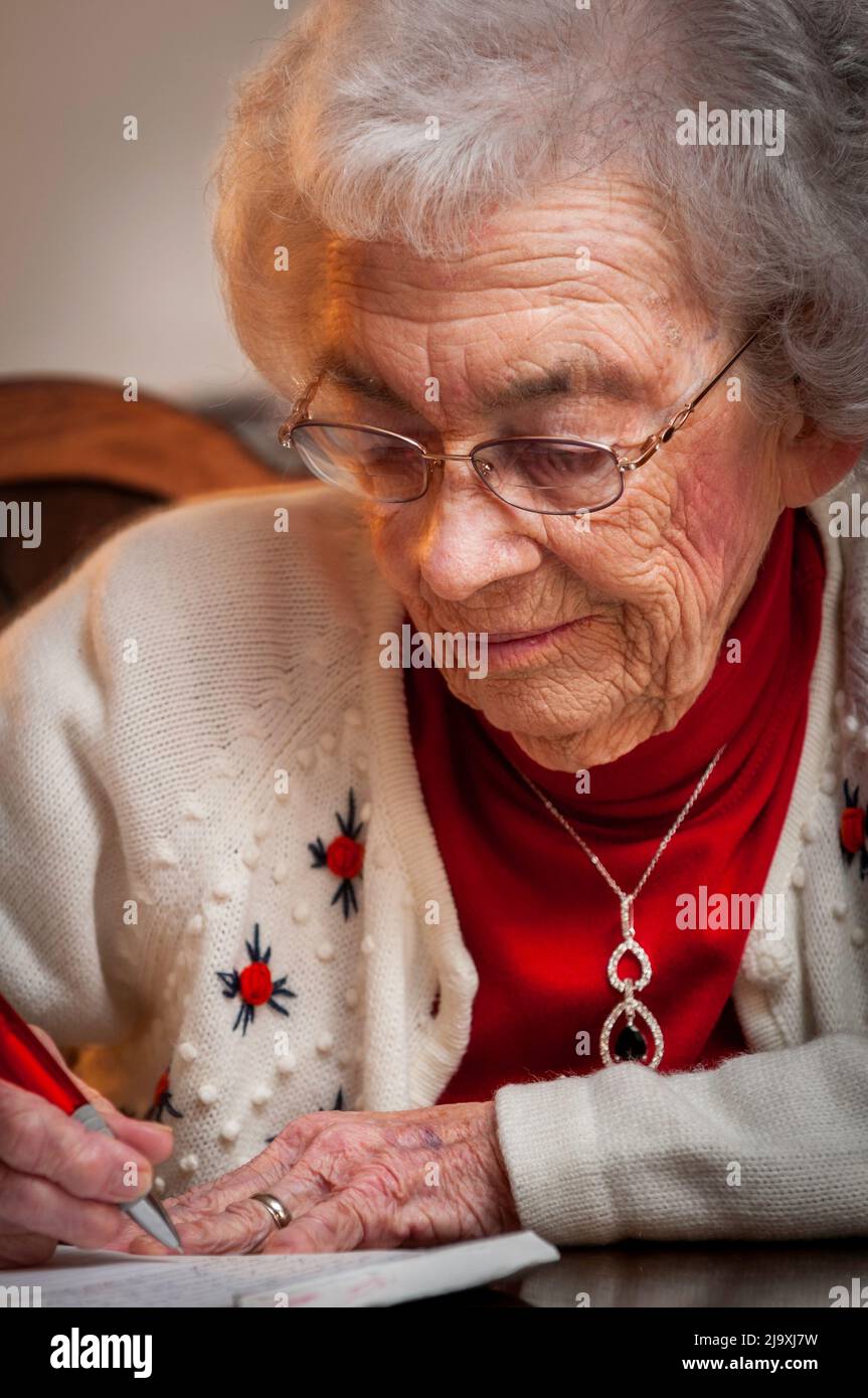Elderly woman sitting at a table and writing a letter Stock Photo